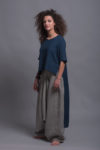 Model wearing the FRIDA linen shirt, emphasizing the shorter front and elongated back hemline with loose-fitting striped harem trousers, highlighting the wide leg and comfortable design.